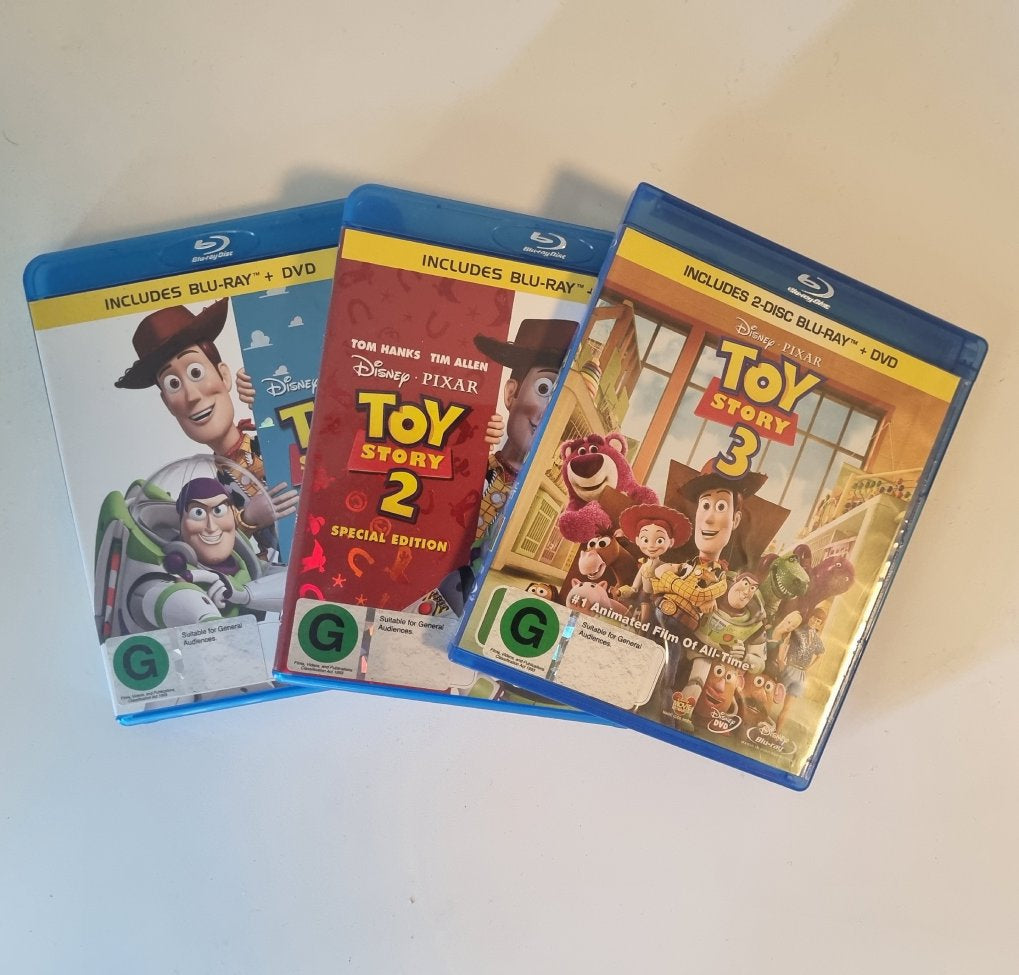 Three 'Toy Story' movie Blu-ray and DVD sets on a white surface.